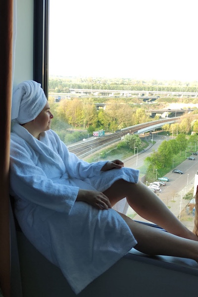 Julia sitzt entspannt am Fenster in einem Bademantel